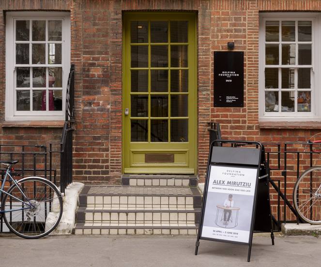 Steps leading from the street to a green and glass door of a brick building.